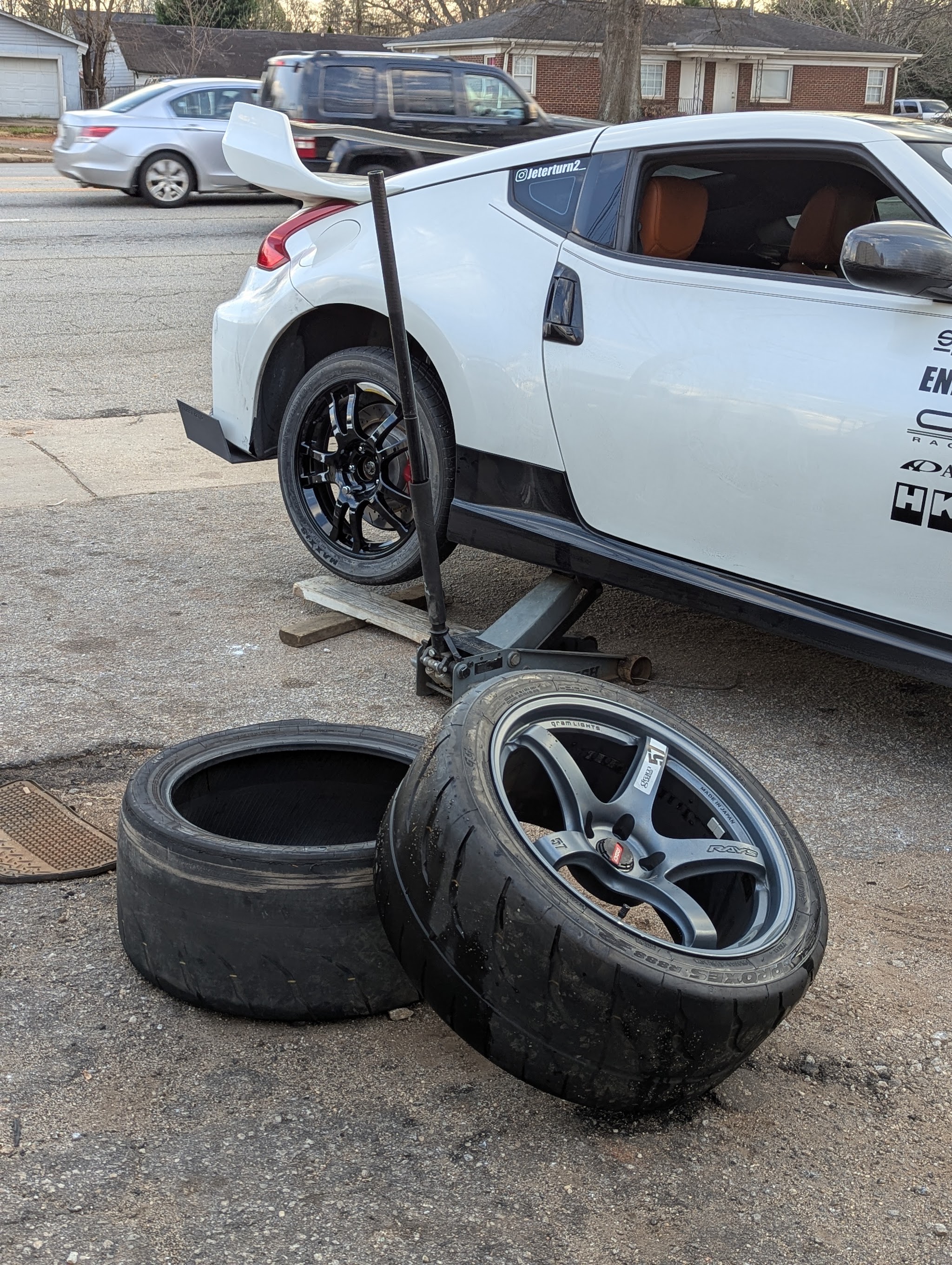 A car jacked up outside the shop with new wheels being fitted and old tires on the ground